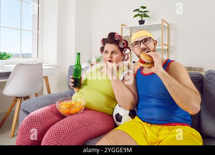 Drôle de couple regardant le sport de football jeu assis sur le canapé à la maison avec la bière et la restauration rapide. Banque D'Images