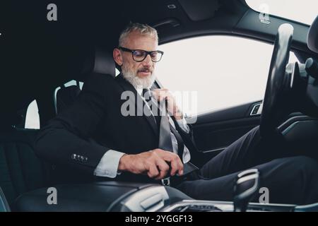 Homme d'affaires portant un costume formel sécurise la ceinture de sécurité dans une voiture moderne mettant en valeur la sécurité de voyage sur la rue de la ville Banque D'Images