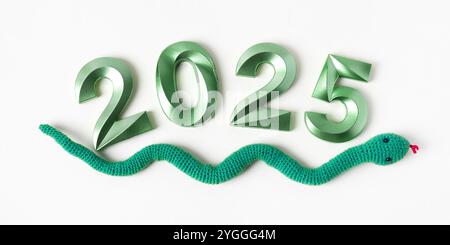 Serpent vert jouet tricoté et numéros verts. Le symbole de l'année 2025 sur fond gris. Banque D'Images