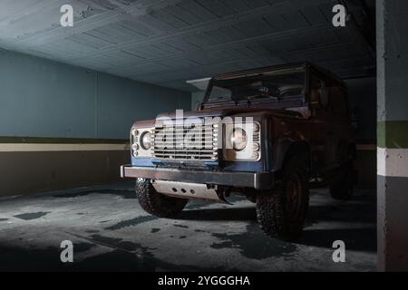 Une voiture de montagne 4x4 classique est garée dans un garage. Il est caché par l'ombre avec le moteur dramatiquement éclairé par la lumière de fenêtre. il y a trace Banque D'Images
