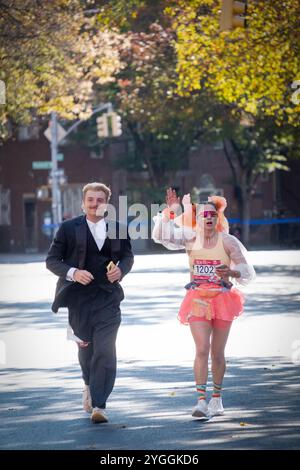 Un couple qui court le marathon de New York 2024 en costumes et tient un téléphone portable. Sur Bedford Ave à Williamsburg autour de la marque de 10 miles. Banque D'Images