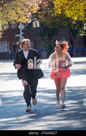 Un couple qui court le marathon de New York 2024 en costumes et tient un téléphone portable. Sur Bedford Ave à Williamsburg autour de la marque de 10 miles. Banque D'Images