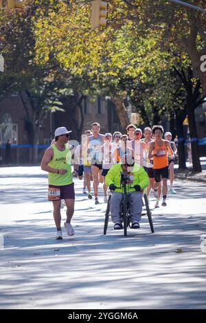 Dans le marathon de NY 2024, un groupe d'élite de coureurs derrière un athlète en fauteuil roulant avec son guide international d'Achille. À la marque de 10 miles à Brooklyn. Banque D'Images