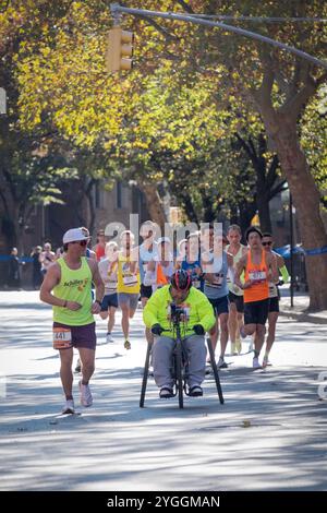 Dans le marathon de NY 2024, un groupe d'élite de coureurs derrière un athlète en fauteuil roulant avec son guide international d'Achille. À la marque de 10 miles à Brooklyn. Banque D'Images