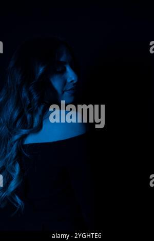Portrait d'une silhouette mystérieuse d'une jeune femme debout sur un fond bleu brillant Banque D'Images