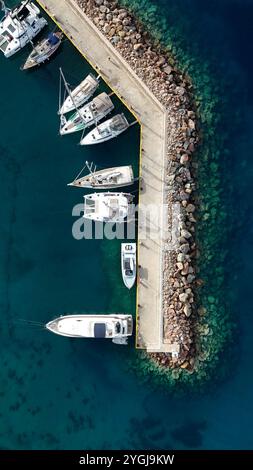 Vue aérienne des yachts de luxe amarrés le long du brise-lames courbé avec des eaux méditerranéennes turquoises et un rivage rocheux Banque D'Images