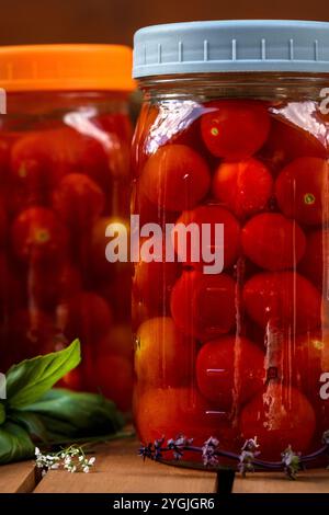 Comptoir en bois de chariot de jardin et bocaux maçon avec tomates cerises en fermentation et chou, entouré de basilic frais et de feuilles de basilic thaï et chapeau de paille Banque D'Images