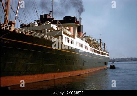 TSS Monowai accosté dans le port de Sydney. Le TSS Monowai accoste au port de Sydney. Ce paquebot légendaire, connu pour son service transtasmanien entre la Nouvelle-Zélande et l'Australie, est capturé ici avec sa coque noire distinctive, son entonnoir rouge et ses canots de sauvetage le long du pont supérieur. Le TSS Monowai a joué un rôle crucial dans les voyages et les transports maritimes au milieu du XXe siècle. Cette image offre un regard nostalgique sur l’un des navires les plus importants de l’époque, qui reliait les principaux ports du Pacifique Sud. Banque D'Images