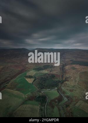 Vue aérienne spectaculaire d'un paysage sombre sous des nuages sombres, avec des collines ondulantes, des terres agricoles et des routes de campagne sinueuses. Banque D'Images