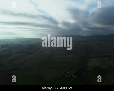 Vue aérienne d'un paysage rural brumeux avec des collines et des terres agricoles sous un ciel dramatique, montrant une scène d'automne sombre et atmosphérique. Banque D'Images