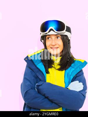 Gros plan femme skieuse porter bleu costume masques chapeau ski veste rembourrée couverture bouche avec snowboard isolé sur l'espace blanc pastel Uni. Hiver extrême Banque D'Images