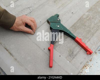 outil de rivetage sur texture de fer vue de dessus et rivet en aluminium tenant la main mâle, dispositif tenu à la main pour poser des rivets lors de l'assemblage de pièces métalliques minces Banque D'Images