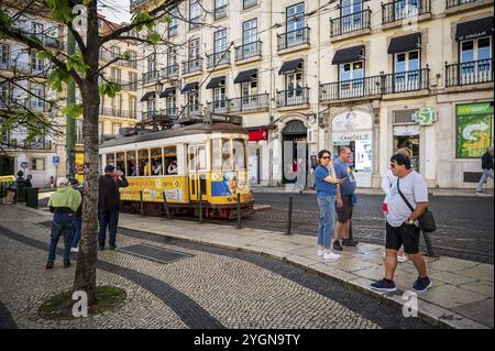 Scène avec un tram en face des bâtiments historiques et les passants en profitant de l'atmosphère de la ville, animé Praca Luis de Camoes avec tram à Lisbonne, Port Banque D'Images