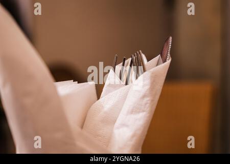 Un serveur prépare de l'argenterie élégante pour dîner dans un cadre de restaurant confortable Banque D'Images