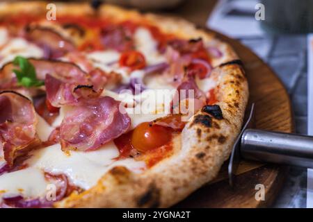 Délicieuse pizza au prosciutto garnie de fromage et de tomates cerises dans un restaurant confortable le soir Banque D'Images