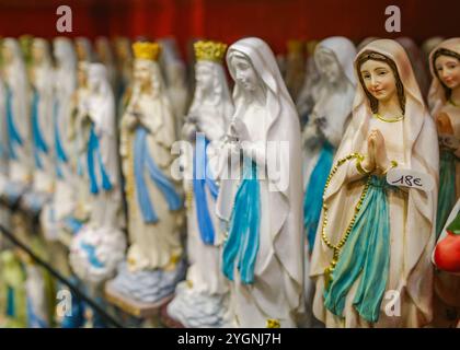 Lourdes, France - 1er novembre 2024 : statues de la Vierge Marie, bougies et autres souvenirs catholiques en vente dans une boutique de cadeaux à Lourdes Banque D'Images