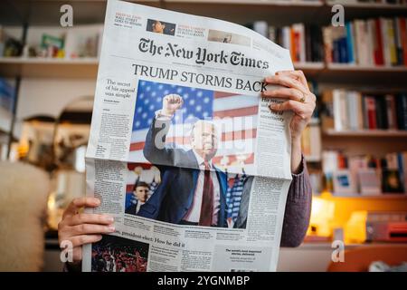 Paris, France - 7 novembre 2024 : femme lisant le New York Times dans un salon confortable, avec Trump Storms en première page couvrant le retour de Donald Trump à la politique américaine Banque D'Images