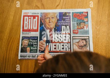 Paris, France - 7 nov. 2024 : garçon tout-petit curieux donnant un coup de pouce à un journal allemand Bild avec le titre Da Isser Wieder - là, il présente à nouveau le retour de Donald Trump à la présidence américaine. Banque D'Images