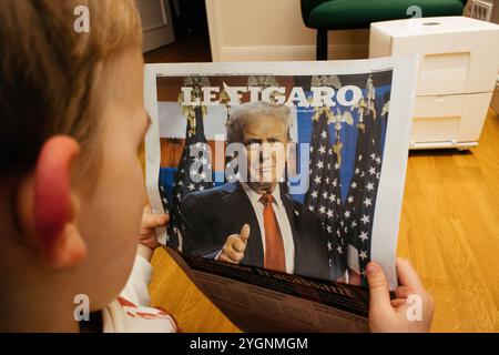 Paris, France - 7 novembre 2024 : un enfant examine attentivement la couverture du Figaro, mettant en vedette la victoire électorale de Donald Trump, reflétant l'attention des médias internationaux sur les élections américaines. Banque D'Images