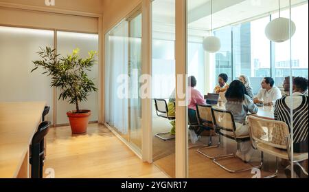 Une équipe diversifiée s'engage dans une réunion au sein d'un bureau moderne esthétiquement agréable. Le cadre dispose d'une salle de conférence spacieuse au décor élégant Banque D'Images