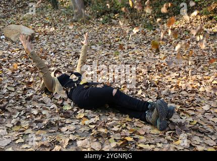 BELEMEDIK, ADANA, TURQUIE-30 OCTOBRE 2016 : femme heureuse non identifiée se couchant sur des feuilles sèches et jetant des feuilles dans l'air au parc national de Belemedik Banque D'Images