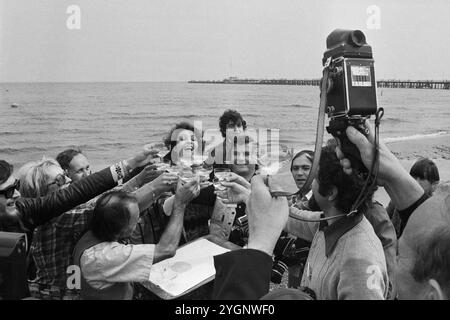 Die rumänische Pop-Sängerin Angela Similea stößt an mit Pressefotografen am Strand von Sopot, WO sie beim Intervision Song Contest 1977 (Sopot 77) zusammen mit Olimpia Panciu und Marius Teicu [Ţeicu] auf den 9. Platz und mit ihrem Solo-Auftritt auf den 18. Platz kam. Rechts neben ihr steht der DDR-Fotograf Tassilo Leher, Polen 1977. Zum Schluss wird mit Sekt gefeiert. Banque D'Images