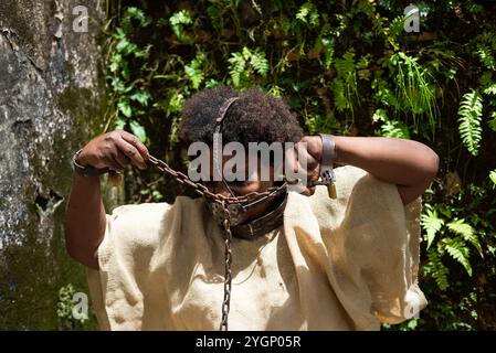 Femme habillée comme une esclave avec un masque de fer sur sa bouche assise en tirant sur ses chaînes. L'esclavage au Brésil. Représentation de l'esclave Anastacia. Banque D'Images