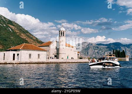 Yacht avec des touristes navigue devant l'église de notre-Dame des rochers sur une île dans la baie de Kotor. Monténégro. Photo de haute qualité Banque D'Images