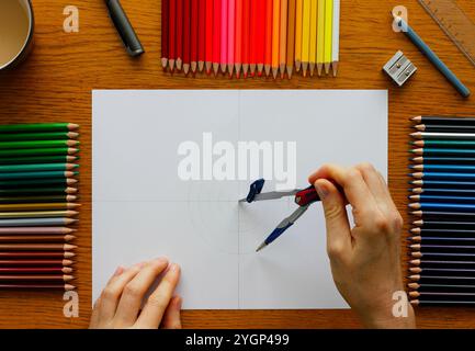 Mains d'une femme caucasienne dessinant des cercles concentriques avec une boussole dans le cadre d'un motif de mandala auto-fabriqué, des ustensiles de dessin et une tasse avec du café Banque D'Images