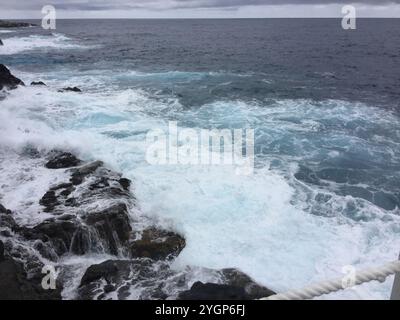 Vagues s'écrasant contre Rocky Shore sous ciel nuageux Banque D'Images