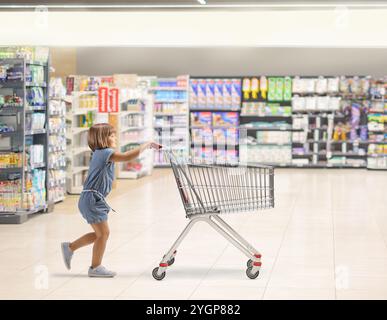 Photo de profil pleine longueur d'une petite fille poussant un panier dans un supermarché Banque D'Images