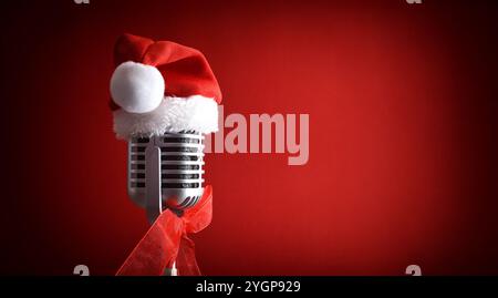 Détail de vieux microphone avec chapeau de Père Noël sur le dessus sur fond dégradé rouge foncé. Vue latérale. Banque D'Images