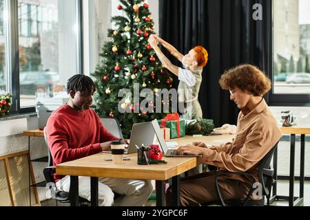 Les collègues apprécient l'esprit des fêtes lorsqu'ils décorent l'arbre du bureau et partagent des sourires. Banque D'Images