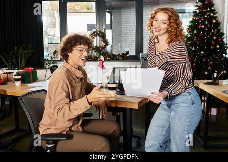 Deux jeunes collègues se livrent à des joies festives tout en célébrant Noël au travail. Banque D'Images