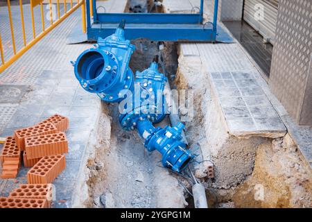 Une vanne d'eau bleue est positionnée à côté d'une tranchée dans une zone urbaine, mettant en valeur les travaux de construction en cours. Banque D'Images