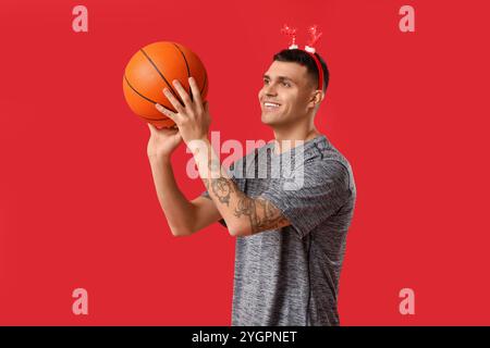 Jeune homme heureux dans des cornes de renne jouant au basket-ball sur fond rouge Banque D'Images