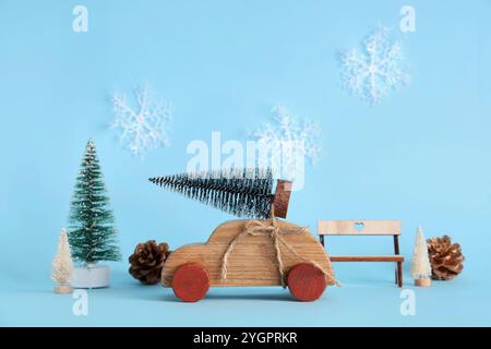 Voiture en bois jouet avec de petits arbres de Noël, des pommes de pin et un banc sur fond bleu Banque D'Images
