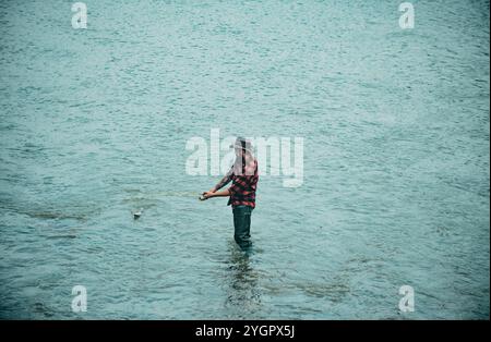 Fisher homme dans l'eau attrapant le poisson, vue de dessus. Pêcheur avec tige, tambour tournant sur la rive de la rivière. Homme attrapant le poisson, tirant la tige tout en pêchant sur le lac. Banque D'Images