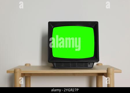 Téléviseur rétro avec écran vert sur table en bois près du mur blanc, espace pour le design. Touche Chroma Banque D'Images