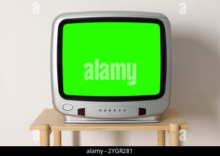 Téléviseur rétro avec écran vert sur table en bois près du mur blanc. Touche Chroma Banque D'Images