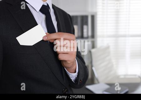 Homme prenant une carte de visite vierge de la poche de sa veste au bureau, gros plan. Maquette pour le design Banque D'Images