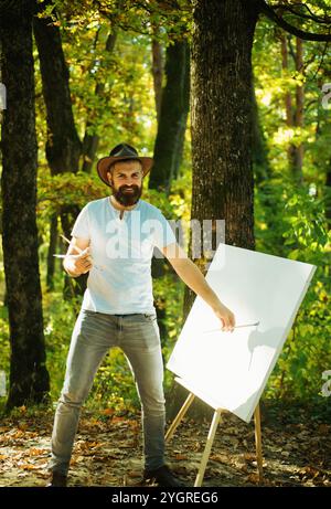 Forêt peintre.Concept d'art.Peinture dans la nature.Démarrer une nouvelle photo.Peintre avec chevalet et toile.Capturez l'instant.Homme barbu peintre à la recherche Banque D'Images