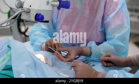 Chirurgiens portant des gommages bleus et des gants stériles pratiquant une chirurgie oculaire sur un patient sous microscope. Banque D'Images