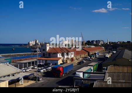 Des activités animées se déroulent le long du port tandis que les véhicules et les bâtiments créent une atmosphère pittoresque de ville côtière. Banque D'Images