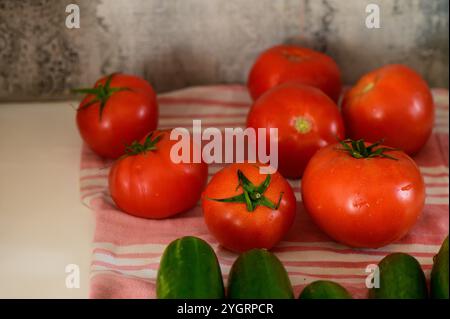 Tomates et concombres fraîchement récoltés disposés magnifiquement sur un chiffon doux et rayé dans une cuisine chaleureuse. Banque D'Images