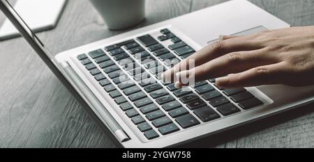 Peau claire et ongles bien manucurés sur une main appuyant sur une touche d'ordinateur portable. L'arrière-plan montre une tasse de café, ajoutant à l'ambiance concentrée et calme de l'espace de travail Banque D'Images