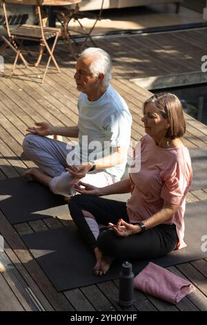 Couple senior méditant sur le patio sur des tapis de yoga, profitant d'une matinée paisible Banque D'Images