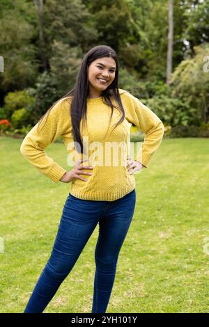 Femme souriante en pull jaune posant en toute confiance dans un parc vert luxuriant Banque D'Images