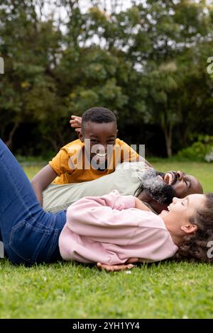 famille multiraciale profitant de moments ludiques ensemble sur l'herbe, riant et se liant à l'extérieur Banque D'Images
