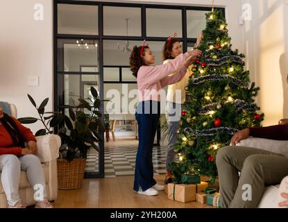 Famille multiraciale décorant l'arbre de Noël ensemble à la maison, profitant de l'esprit festif de vacances Banque D'Images